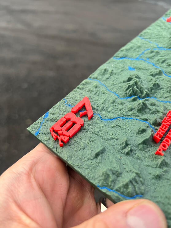 Detail 3D tisku loga B7 na plastické mapě Beskyd, červený 3D text a vrstevnice